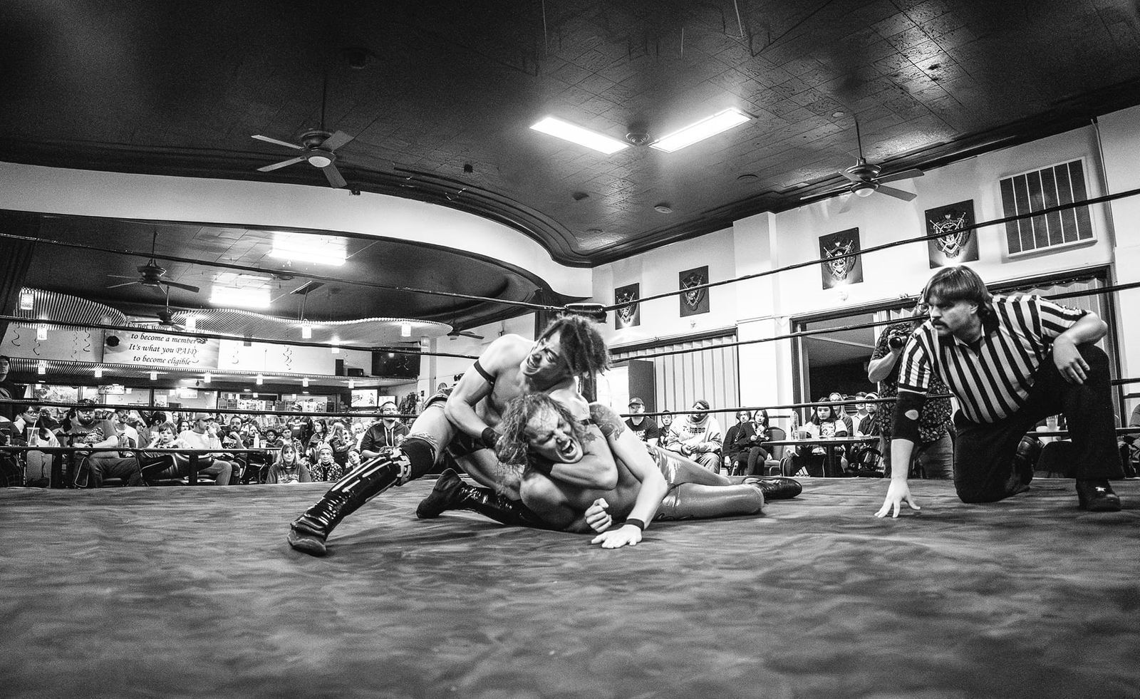 A rare photo of one of the minds behind Ringside Sandwiches being a referee during a wrestling match.

One wrestler has another wrestler in a headlock. 